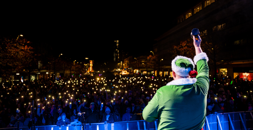 Alex the elf in front of thousands of fans holding up phone torchlights at Plymouth City Centre Christmas Lights Switch On